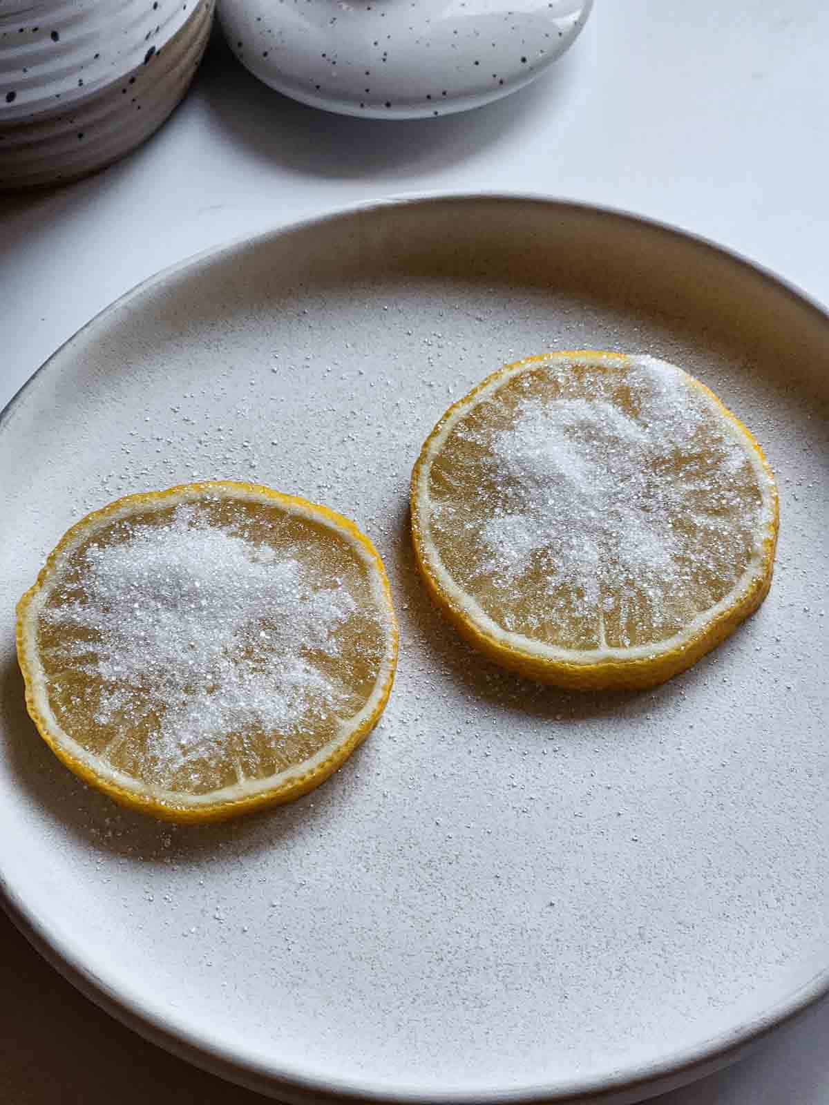 Two lemon slices with sugar on them on a white plate.