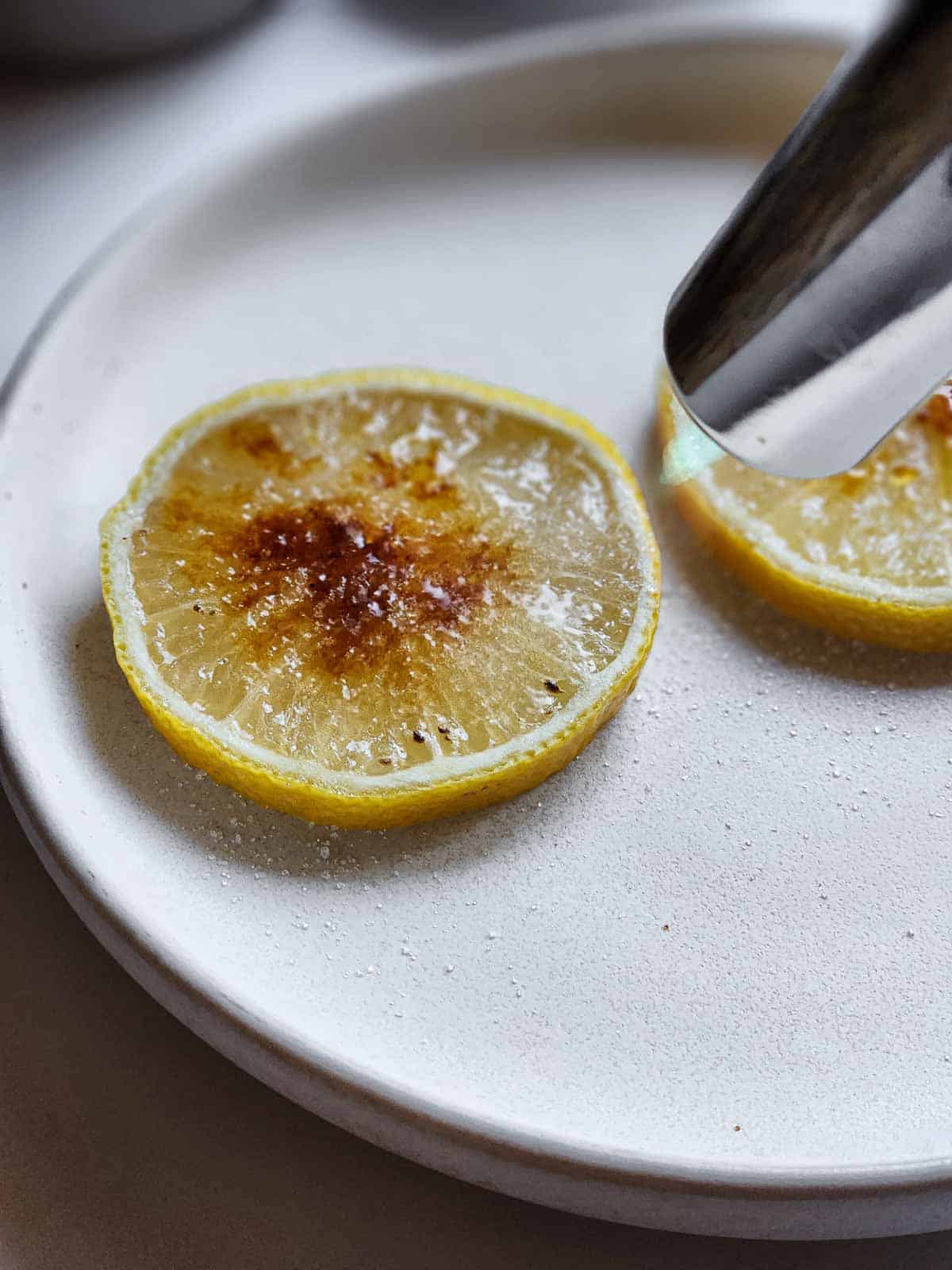 Sugared lemon slices with a kitchen torch pointed at them getting torched.