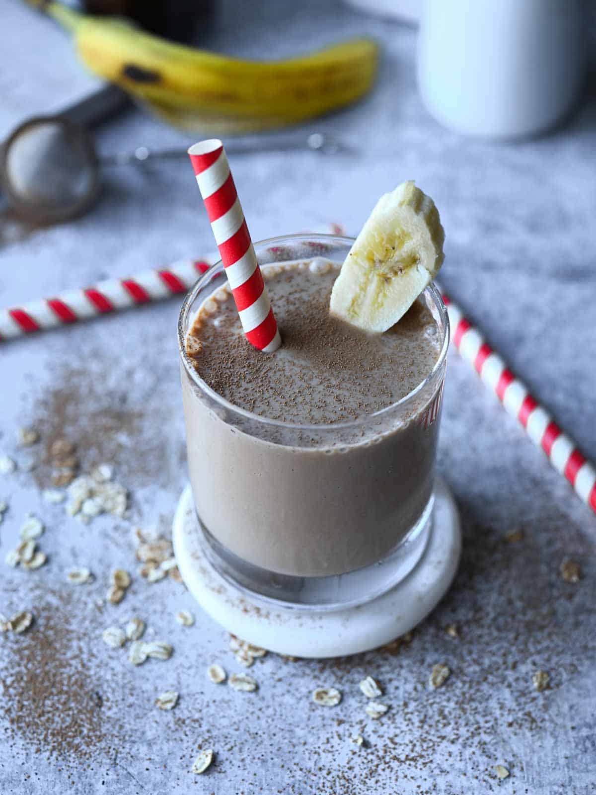 Overview of chocolate tahini oat milk smoothie in a clear glass with a red and white straw.
