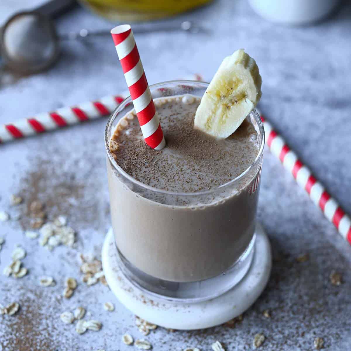 Chocolate tahini smoothie in a clear glass with a red and white straw on a grey surface.