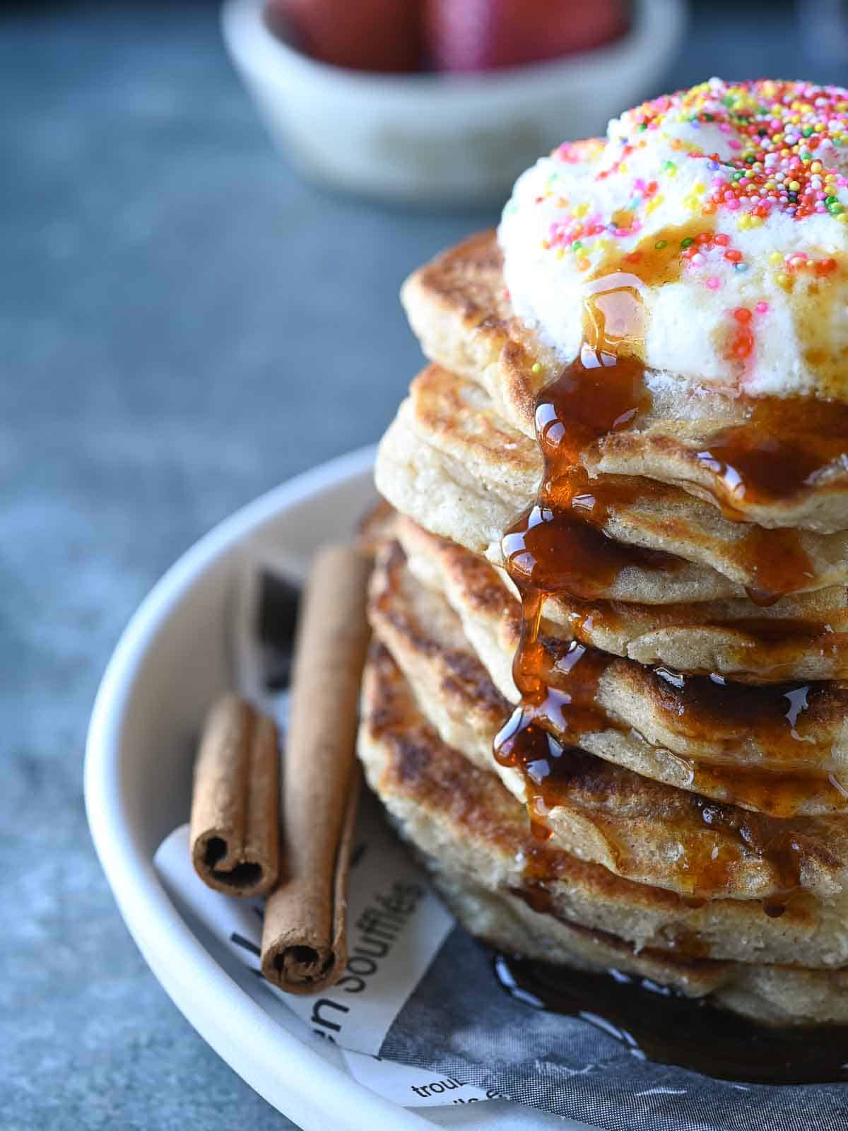 Close-up of sweet cream pancakes with whipped cream and maple syrup dripping down.
