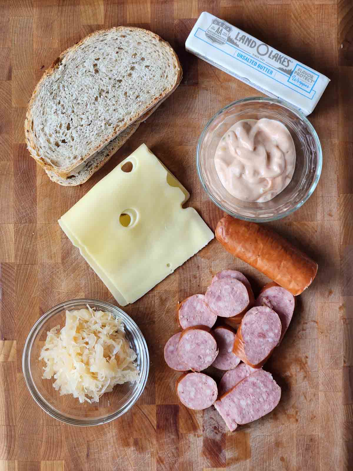 Ingredients for a kielbasa Reuben sandwich on a cutting board.