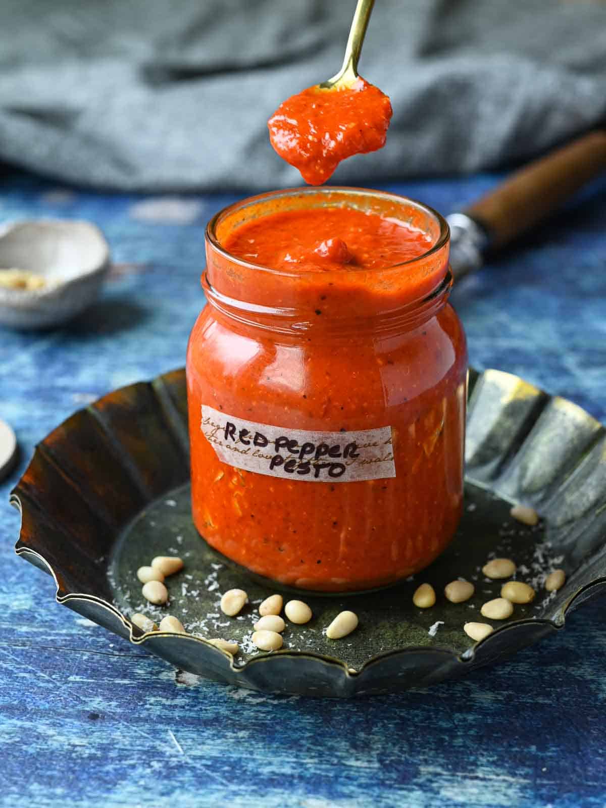 Red pepper pesto sauce in a jar with a spoon in it dripping into the jar.