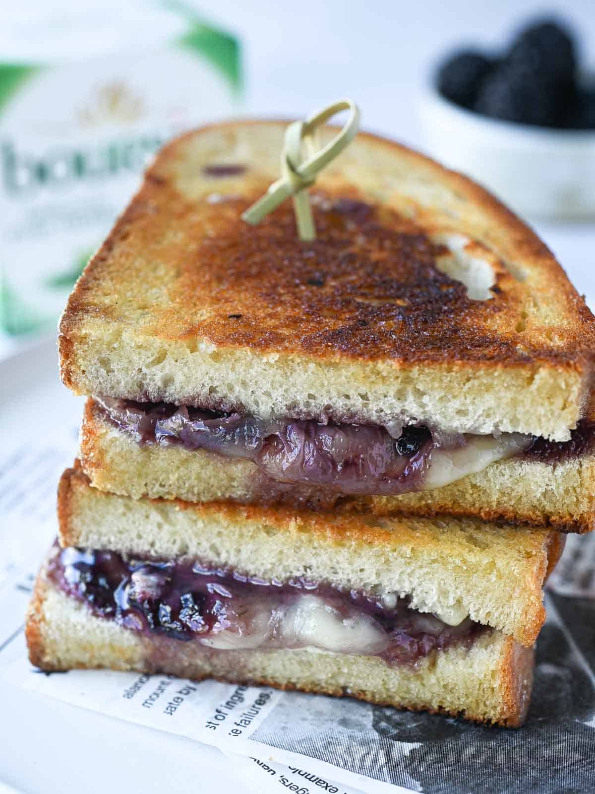 Two stacked blackberry grilled cheese sandwiches on a white plate with Boursin cheese in the background.