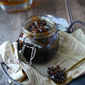 Bourbon and bacon jam in a clear glass jar on a tray lined with brown parchment paper.