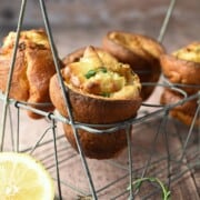 Lemon popovers are suspended in a wire rack with thyme and lemons in the forefront.