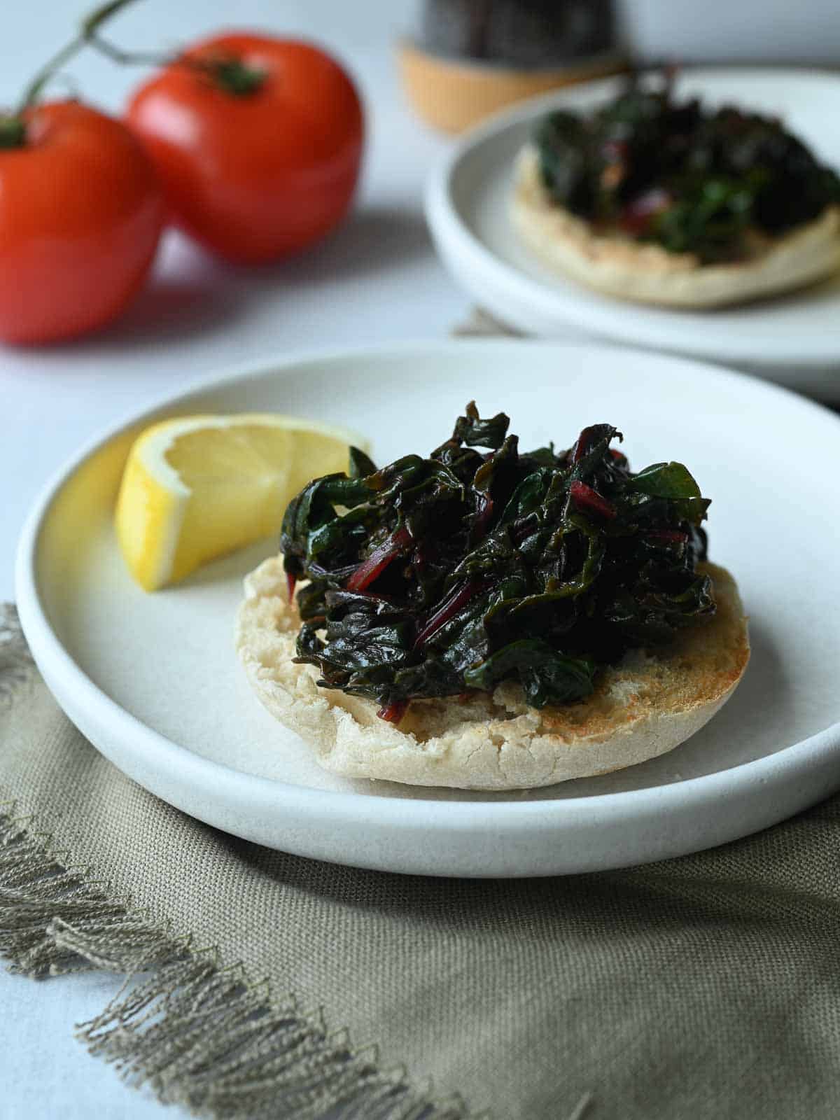 Two white plates with English muffins on them topped with swiss chard.