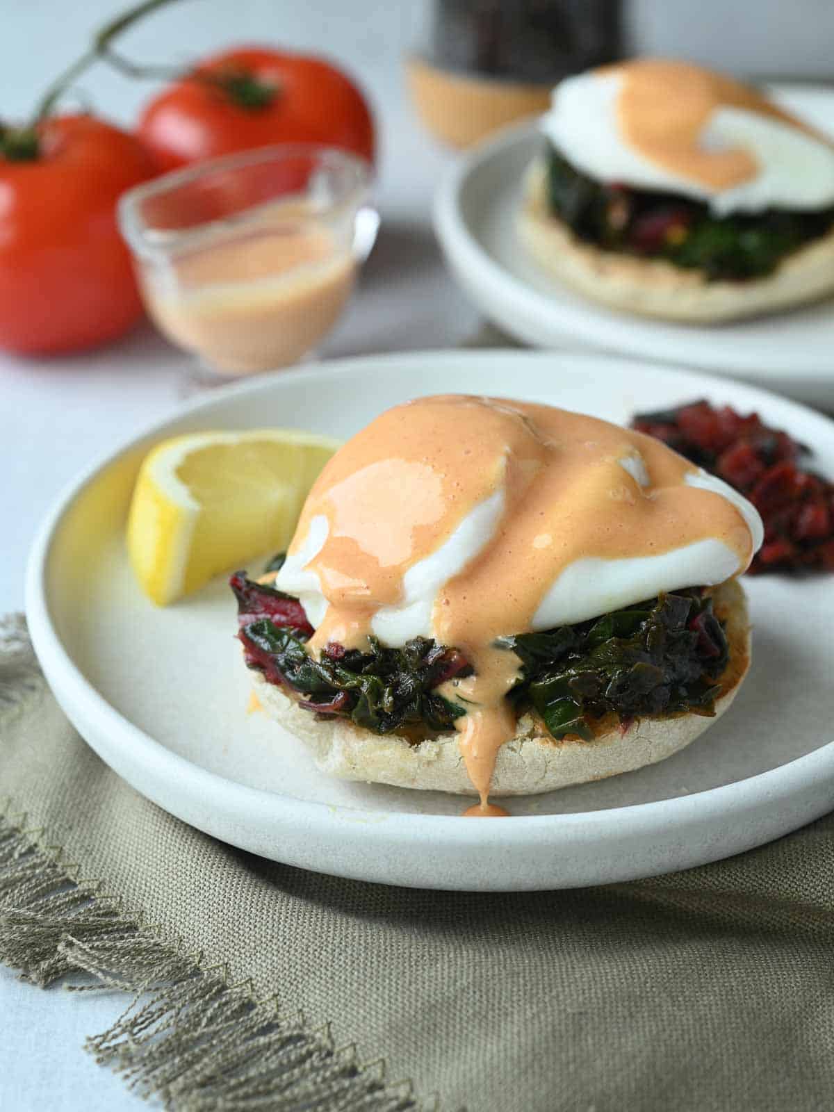 Eggs Florentine topped with tomato hollandaise dripping onto a white plate.