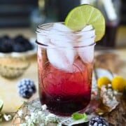 Close-up of blackberry soda in a clear glass with ice and lime.