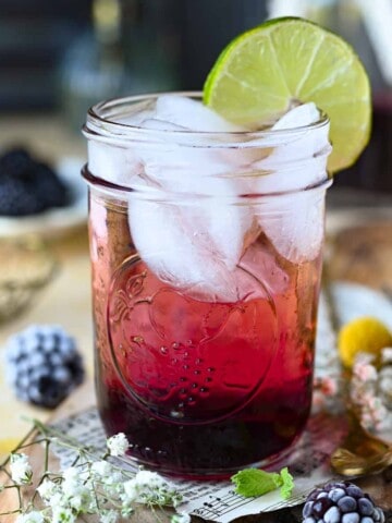 Close-up of blackberry soda in a clear glass with ice and lime.