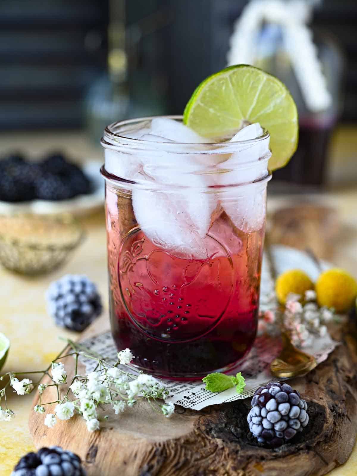 Blackberry soda in a clear glass with lime and blackberries around it.