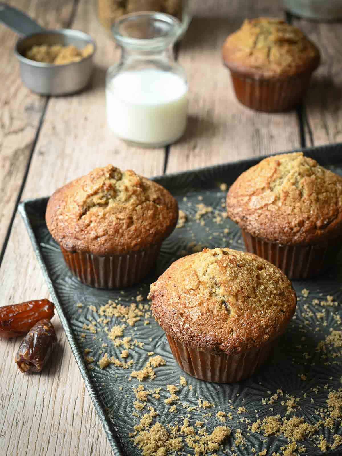 Three date muffins on a metal tray over a wood surface.