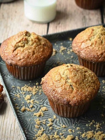 Three date muffins on a textured pan with brown sugar and dates.