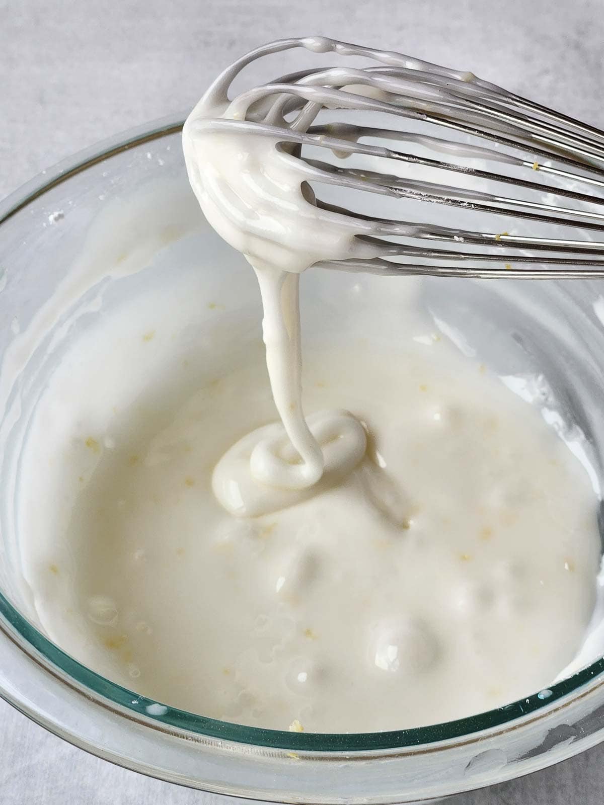 White icing dripping off a whisk into a bowl.