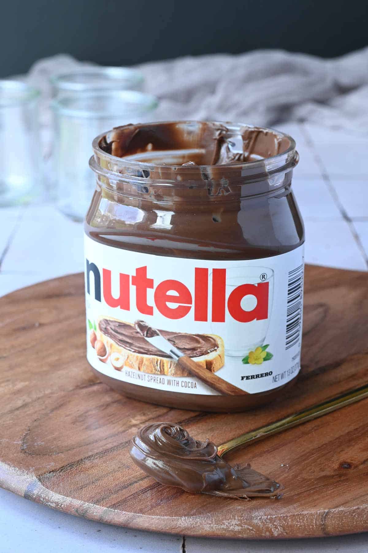 Jar of Nutella on a wood board with a spoon of Nutella next to it.