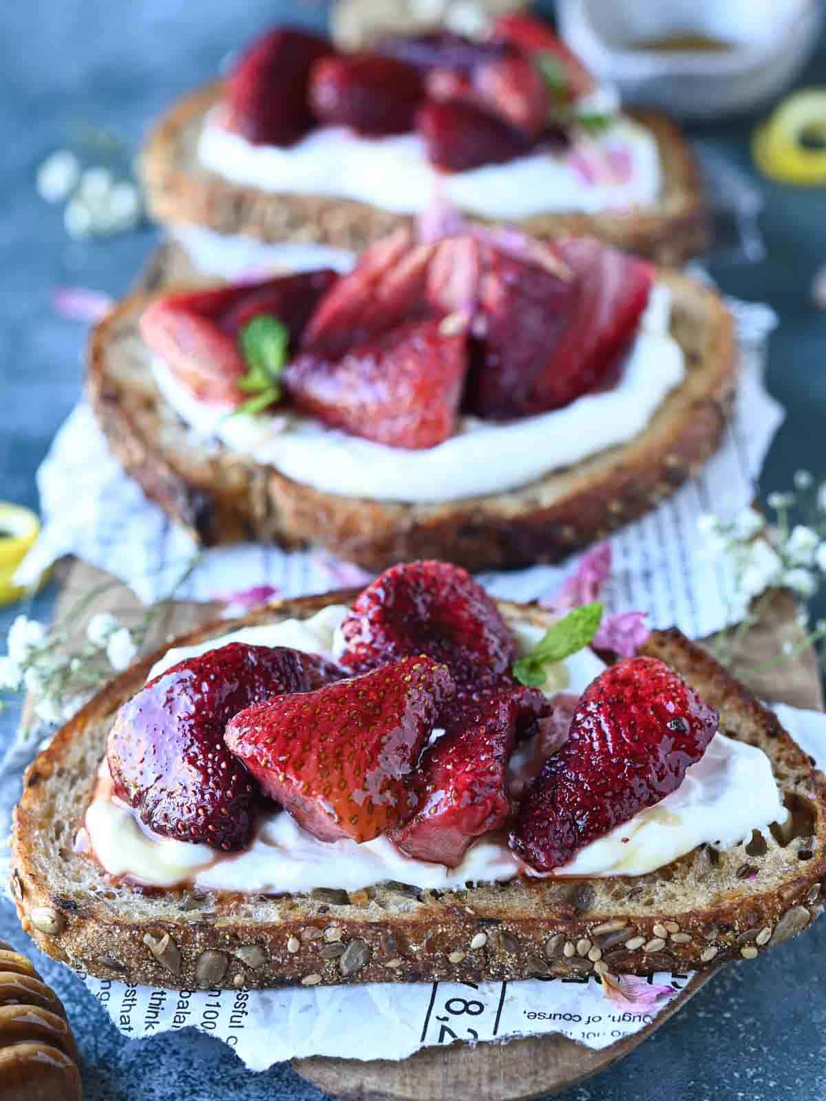 Three slices of labneh toast with strawberries on a blue surface.