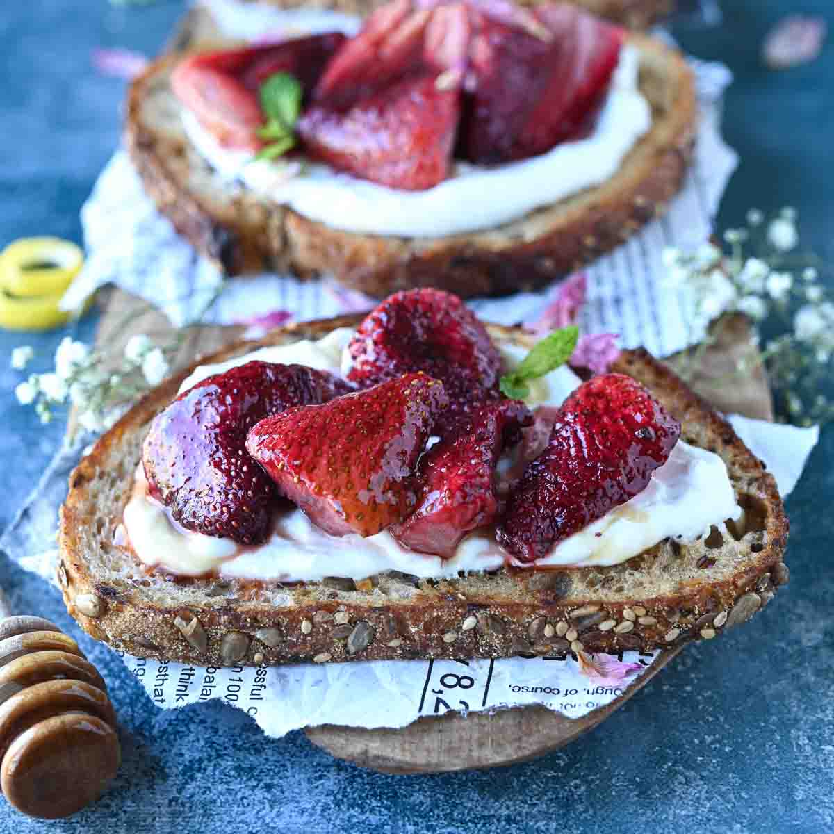 Three gourmet toasts with roasted strawberries and labneh on a blue surface.