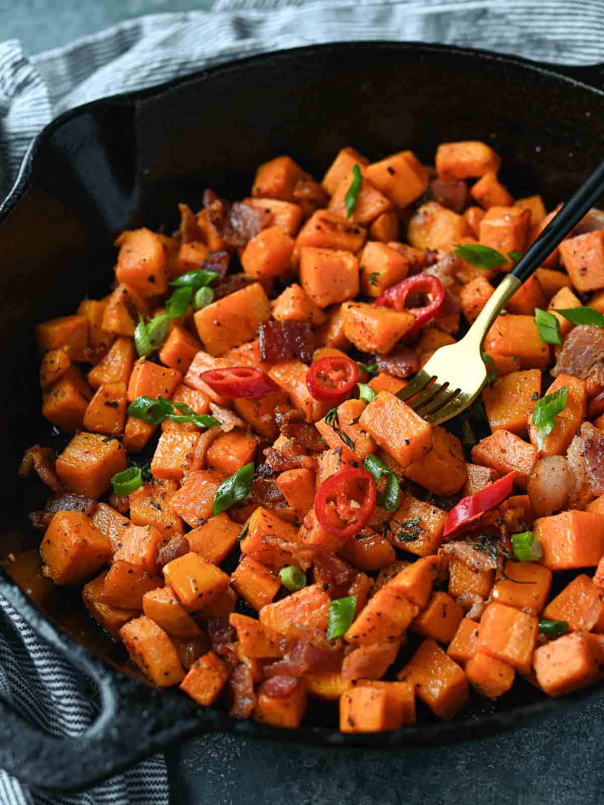 Sweet potato hash in a cast iron skillet with a fork in it.