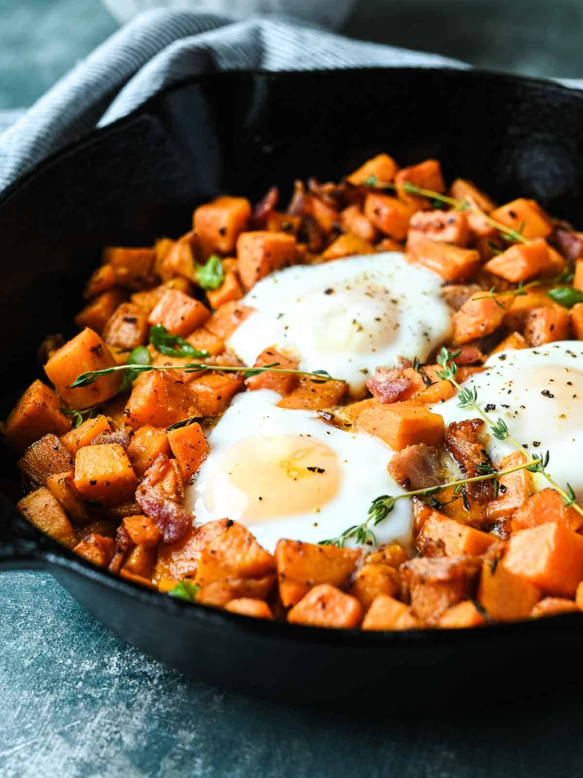 Sweet potato hash in a case iron skillet with 3 fried eggs in it.