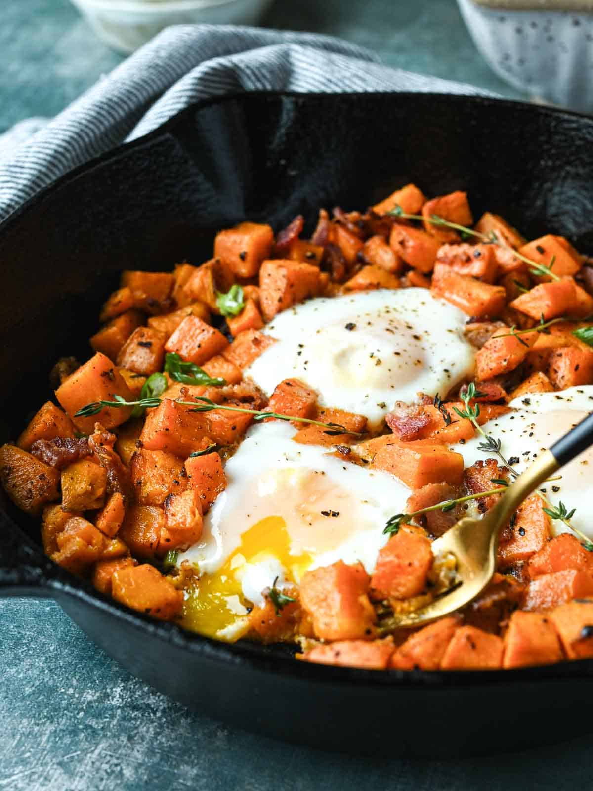 Sweet potato and bacon hash in a skillet with thyme sprigs on top.