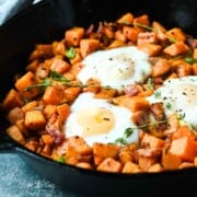 Close-up of sweet potatoes and bacon hash in a skillet with thyme sprigs on top.