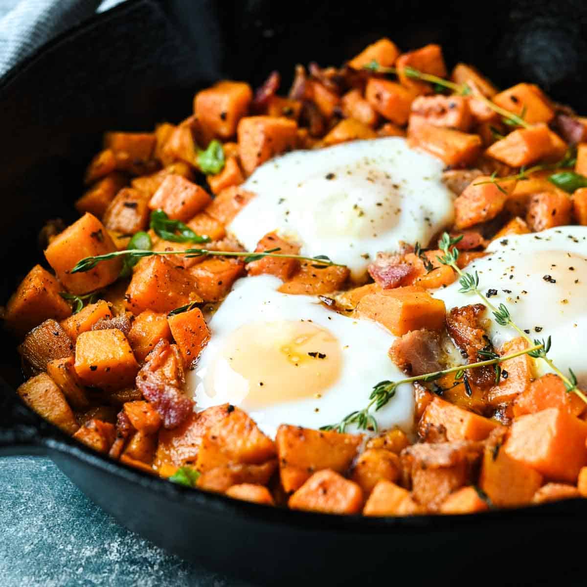 Sweet potatoes and bacon in a cast iron skillet with 3 fried eggs.