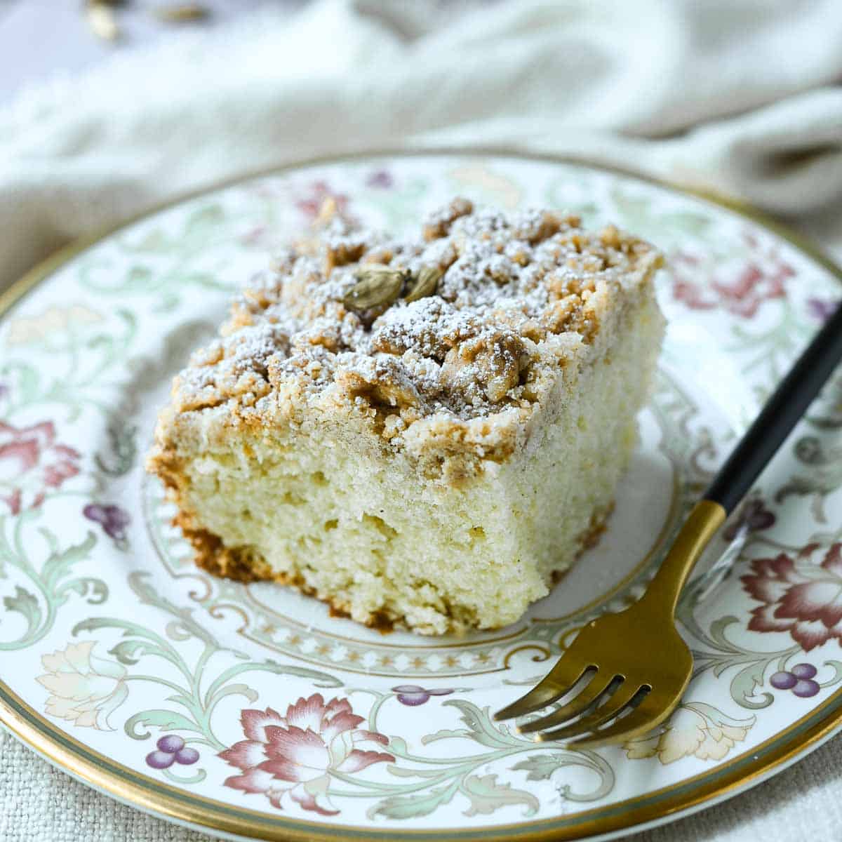 Slice of coffee cake on a flowered plate with a fork to the right.