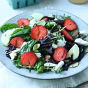 Strawberry salad with goat cheese and lettuce on a white plate.