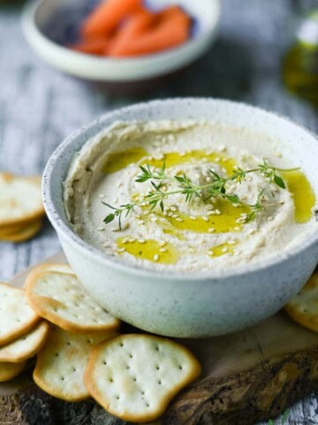 Butter bean hummus in a white bowl, with crackers around it.