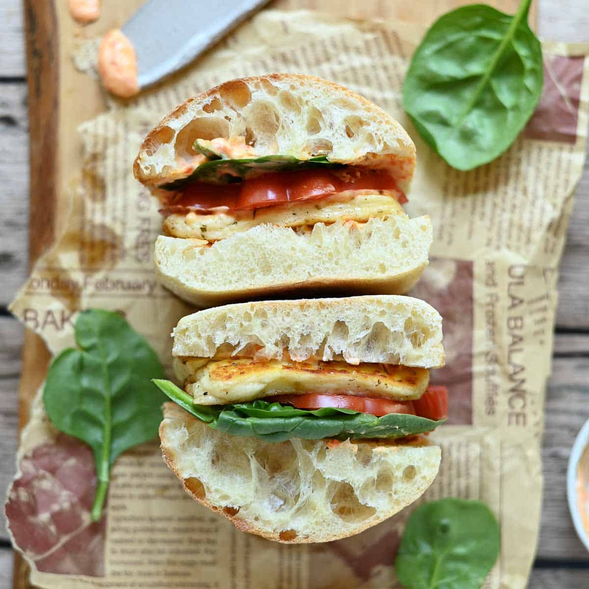 Overview of a two halloumi and tomato sandwiches on parchment paper.
