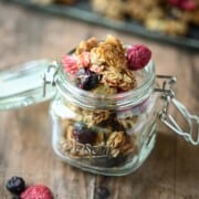 Close-up of berry granola in a clear mason jar on a wood surface.