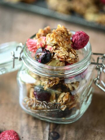 Close-up of berry granola in a clear mason jar on a wood surface.