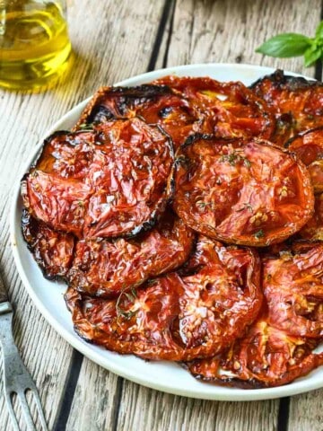 Roasted Beefsteak tomato slices on a white plate with a fork to the left.