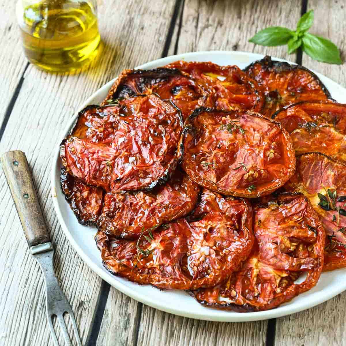 A plate of sliced roasted tomatoes on a wood board with a fork to the left.