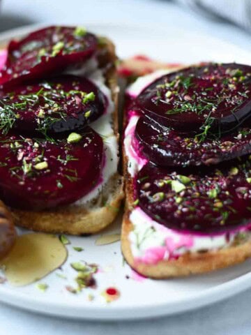 Eye-level view of sliced beets on toast with dill and pistachios.