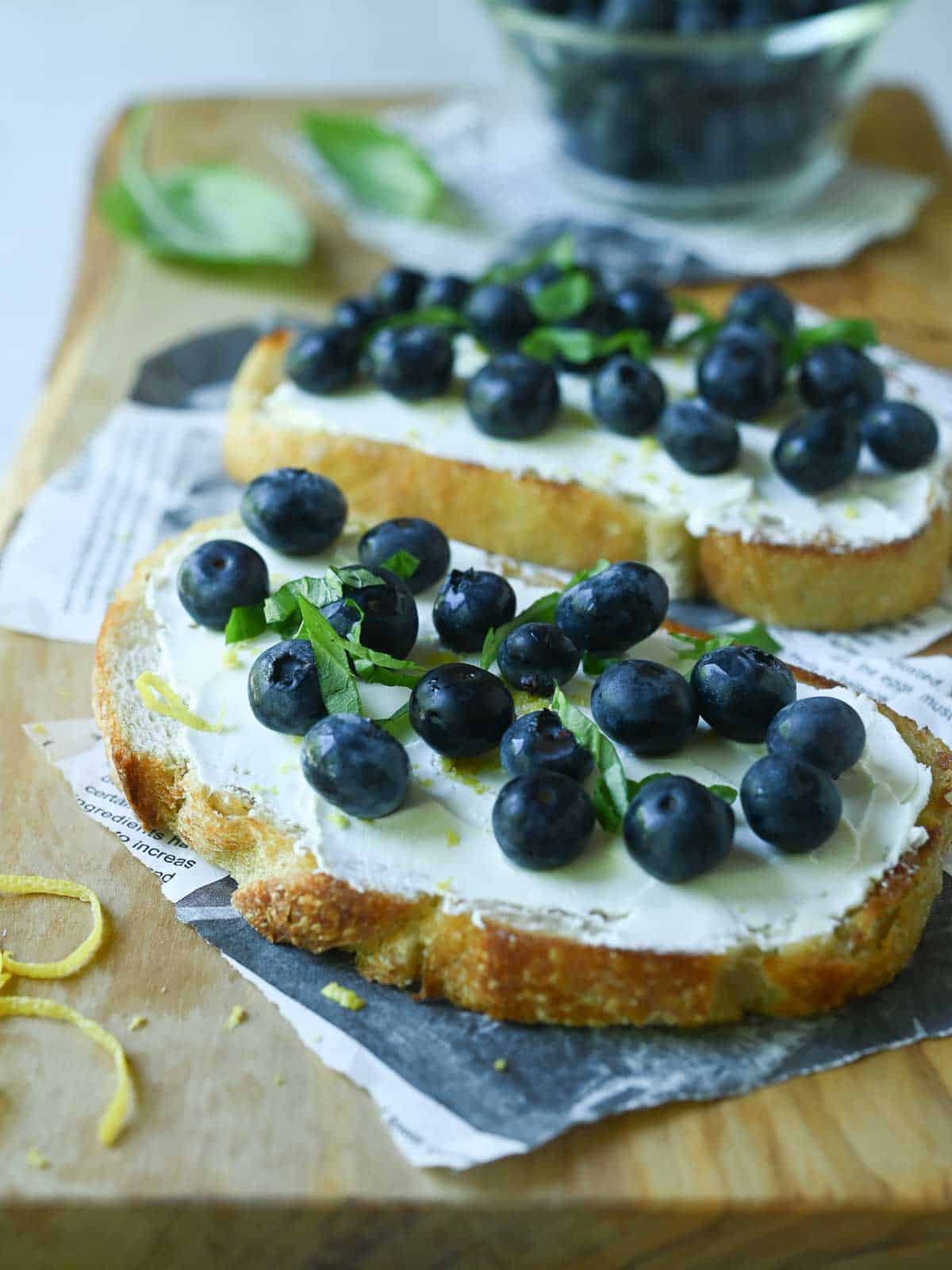 Two blueberry toasts on a wood board.