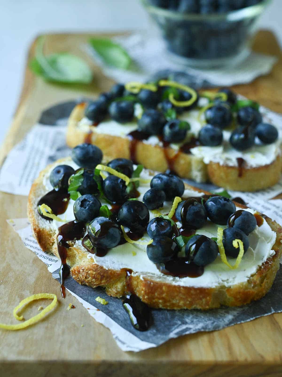 Two blueberry toasts on a wood board with date syrup drizzled on them.
