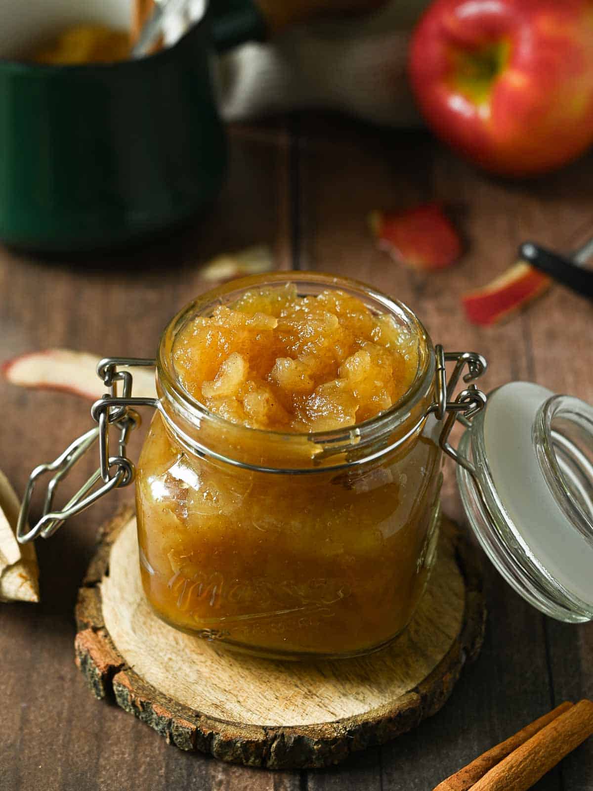 Honeycrisp applesauce in a clear Mason Jar on a wood surface with an apple in the back.