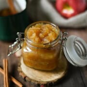 Applesauce in a clear jar with cinnamon sticks next to it.