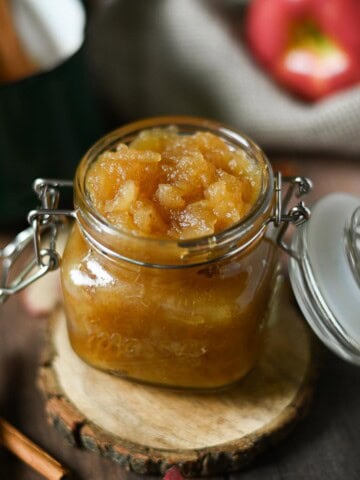 Applesauce in a clear jar with cinnamon sticks next to it.