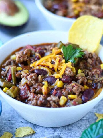 Chili in a white bowl with shredded cheese and a tortilla chip.