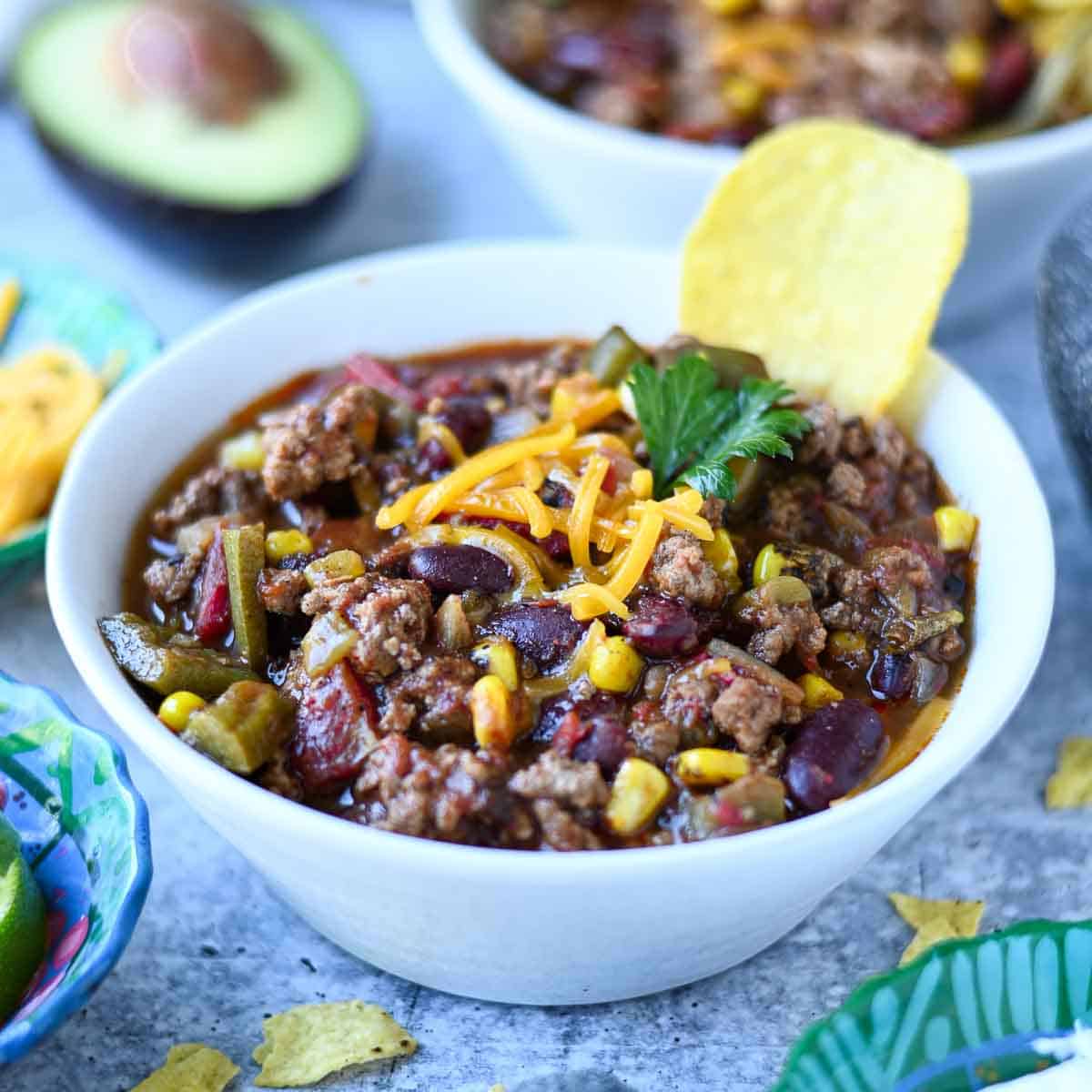 Bowl of chili with a tortilla chip in it on a blue surface.