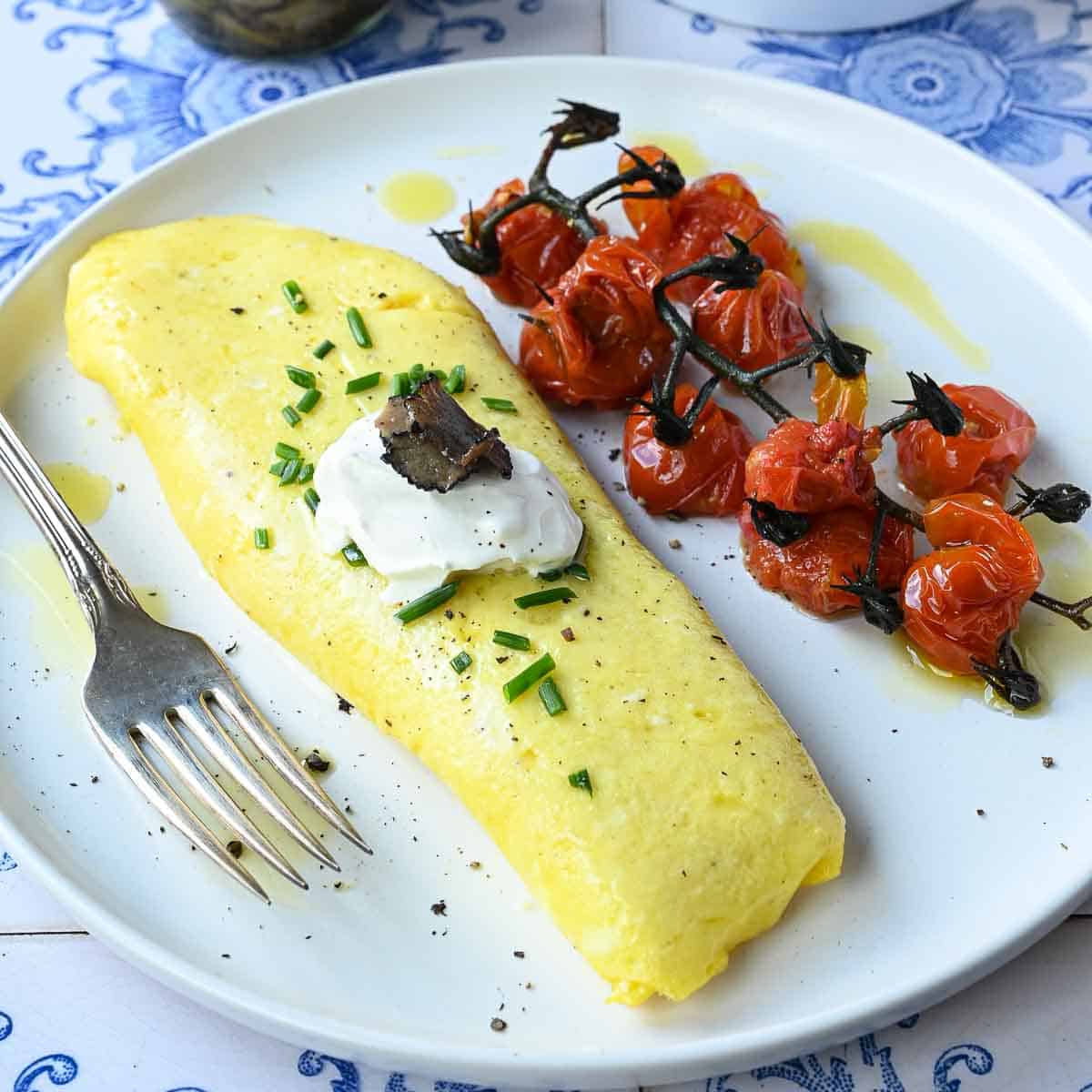 French omelet on a white plate with tomatoes.