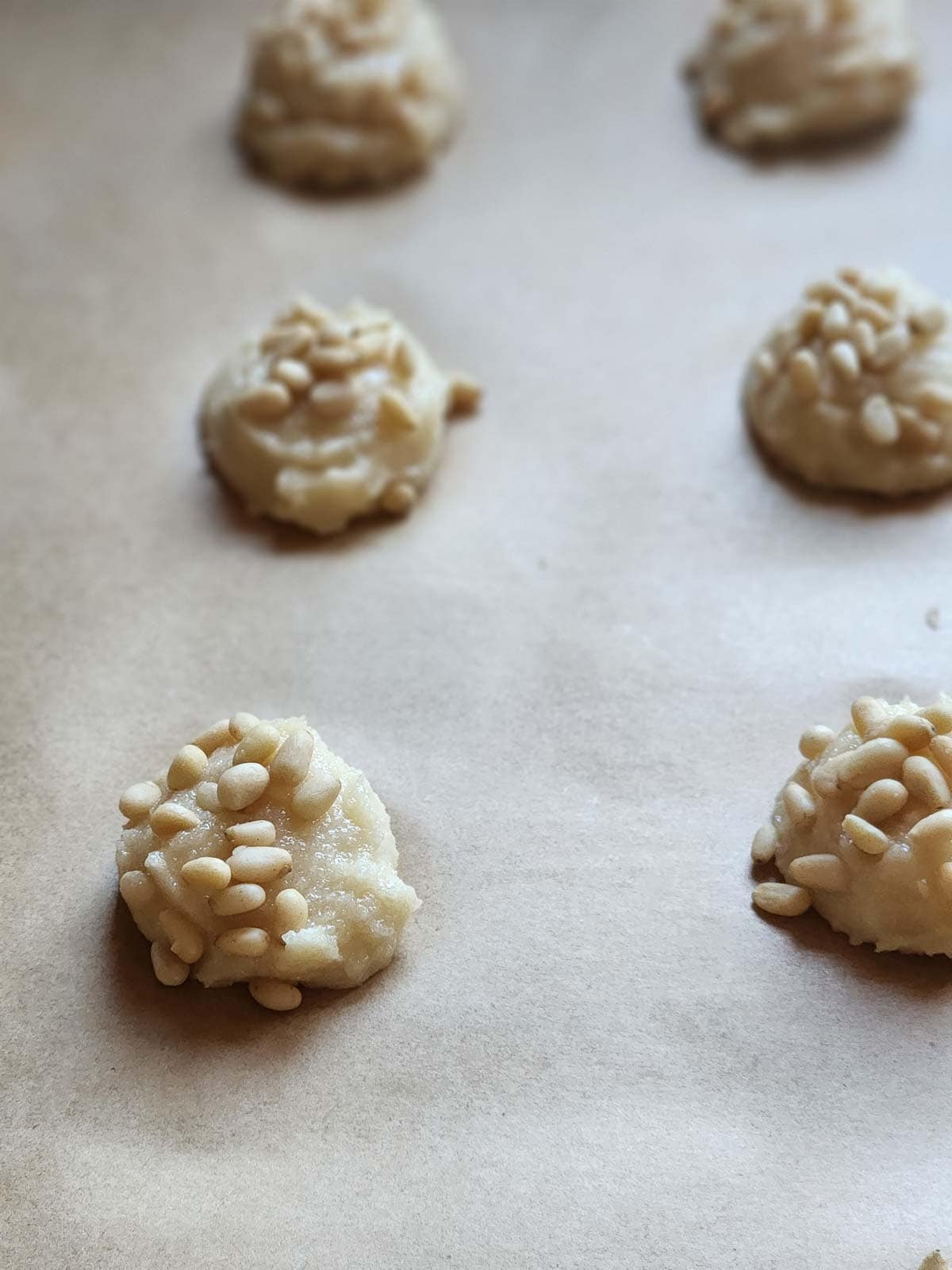 Scoops of cookie batter with pine nuts on parchment paper.