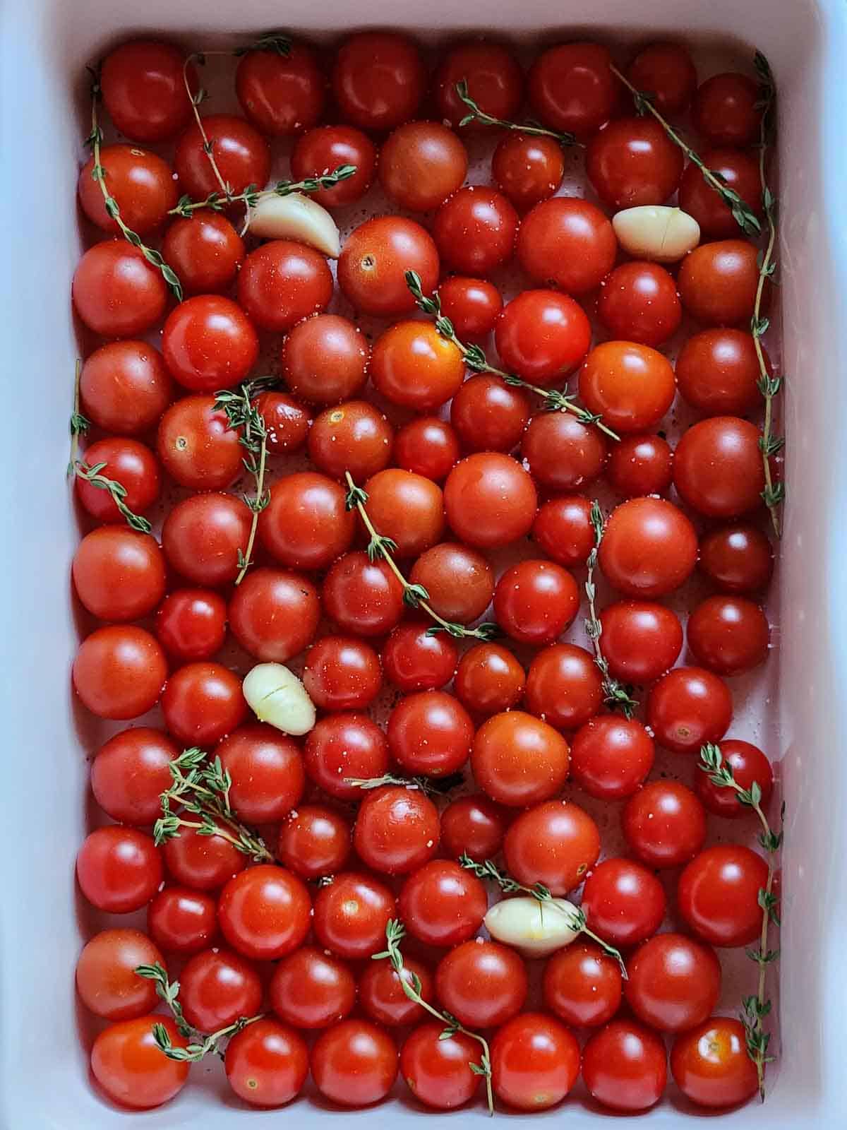 Tomatoes with garlic and thyme in a white baking pan.