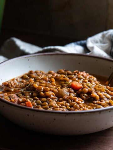 Lentil soup in a beige bowl with a spoon in it.