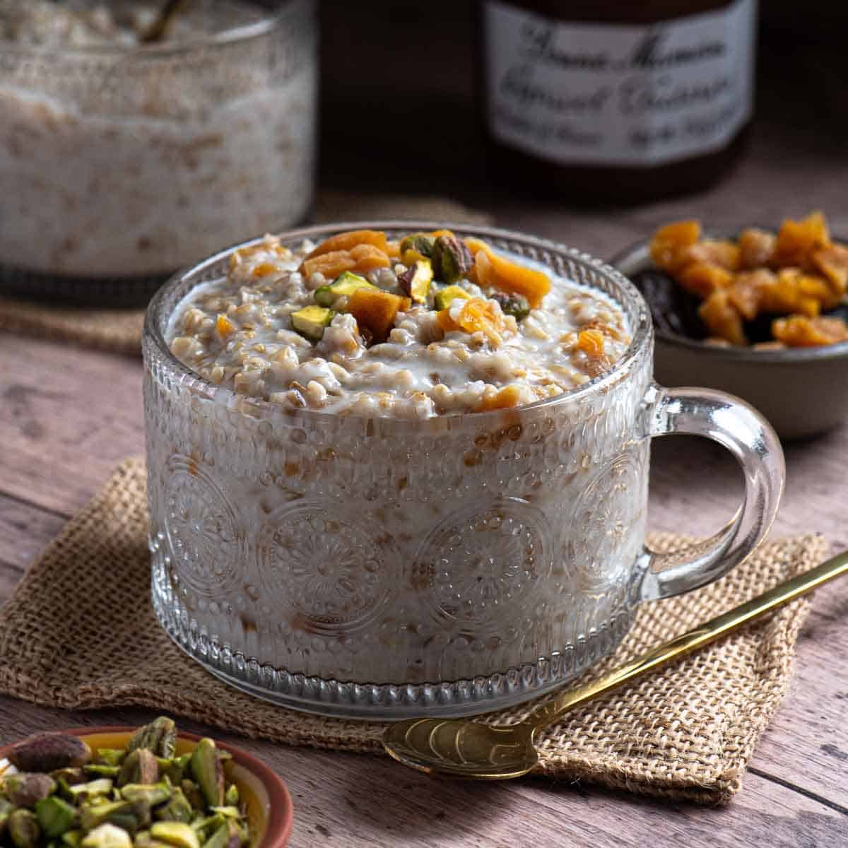 A large clear mug of apricot oatmeal on a wood surface.