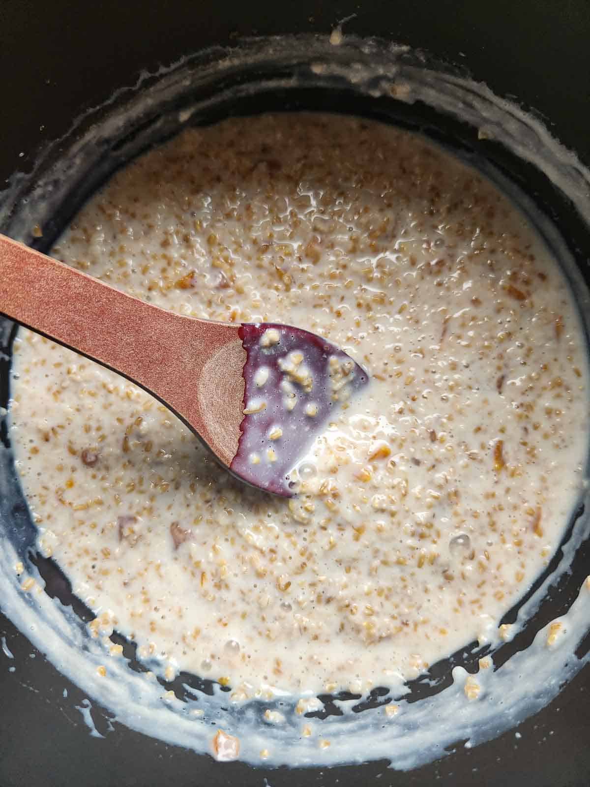 A spoon stirring oatmeal in a pot.