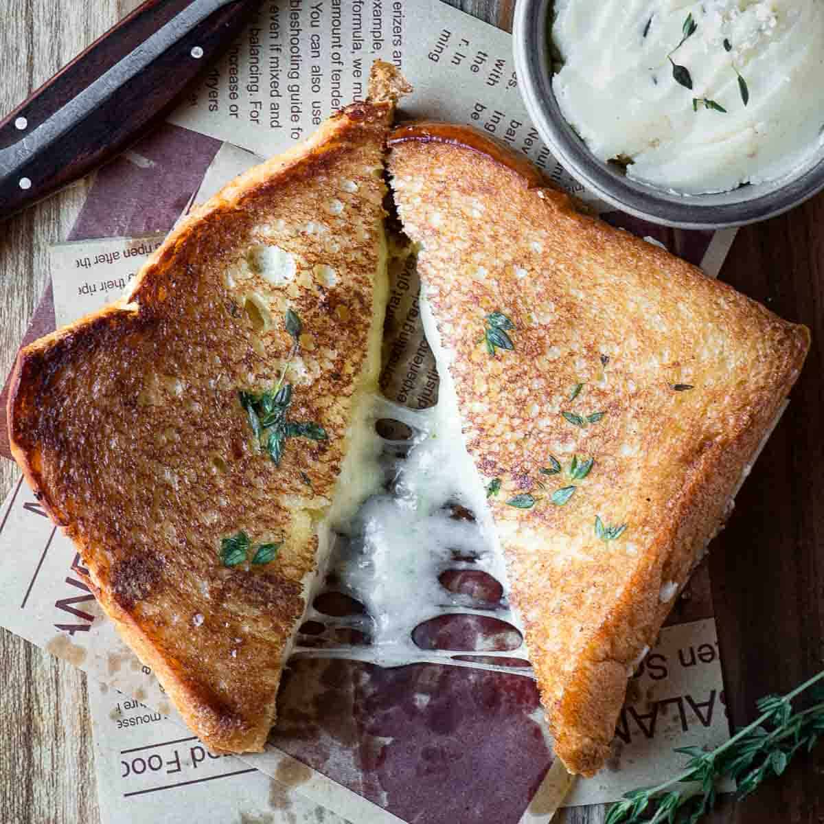Dijon Butter Brioche Grilled Cheese 12 Overhead of a brioche grilled cheese cut in half on a wood surface, showcasing melted cheese and golden-brown brioche.