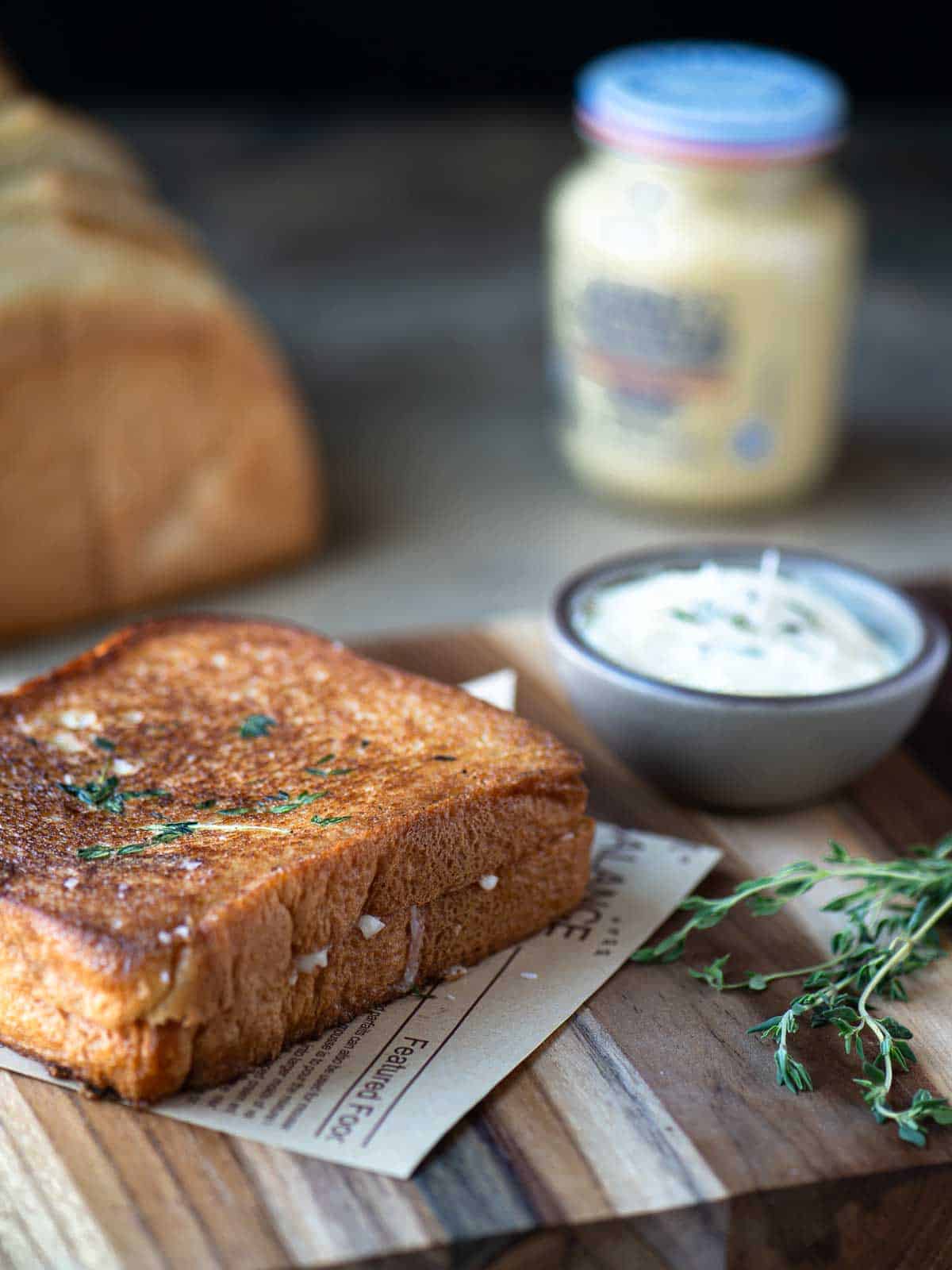 Grilled cheese on a wood surface with butter and mustard in the background.